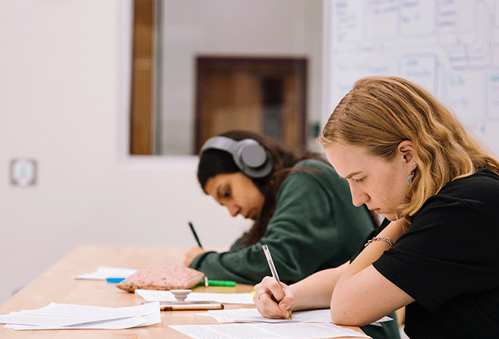 Students working on their assignments in the library, one student is listening music while doing it.